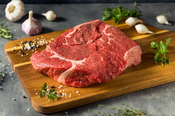 Prime rib cooked beautifully on a white plate, resting on a wooden dining table.